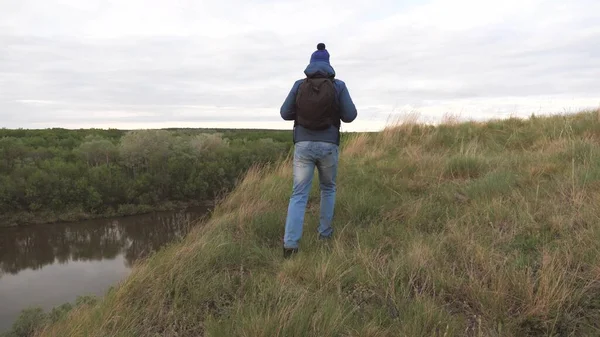 Een man reist met een rugzak op een berg bij de rivier. De man is op zoek naar avontuur. Een weekend op een sportieve wandeling alleen. Rust uit in de natuur. Toeristische verkenning van het gebied — Stockfoto