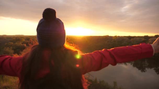 一个伸出手来的年轻姑娘在日落时感到很自由.天空背景下的女冒险家。用背包进行研究工作。周末徒步旅行游客在地面上。生活中的欢乐 — 图库视频影像