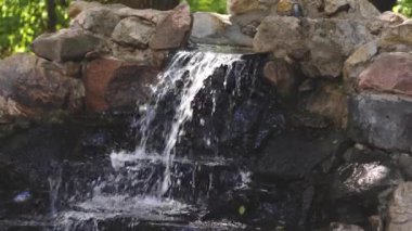 Saf temiz su doğadaki taşlardan yavaşça akar. Uçan spreyli küçük şelale