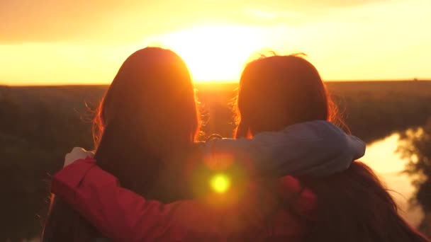 Flickor kramas och titta på solnedgången. Resan är en vandringskollega. Vänner är vänner tillsammans. Beundra soluppgången utanför. Lagarbete. Familjehelg tillsammans vid den strömmande ån — Stockvideo