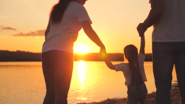 Little daughter jumping holding hands of dad and mom at sunset. Happy family life concept. A child with his parents plays together in flight. Mother and father on a walk with the kid. Spend the — Stock Video