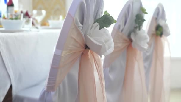 Декор з білими трояндами і рожевими стрічками на порожніх білих стільцях в підготовці до весільної церемонії. Барвистий декоративний фон весільна церемонія святкова концепція — стокове відео