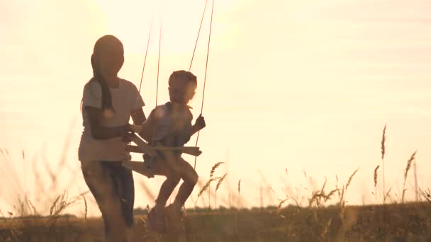 Conceito de sonho parque de diversões. Menina feliz balançando em um balanço no parque ao pôr-do-sol. criança brinca com balanço de madeira, sonho de infância, voo piloto de avião para o céu. Uma família feliz — Vídeo de Stock