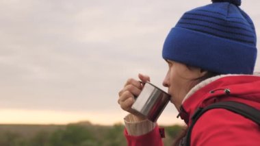 Kız yüksek bir dağda oturan bir kupadan çay içiyor ve parkta doğanın tadını çıkarıyor. Macera arayan bir kadın gezgin. Yürüyüşte rahatla. Uzun mesafeli yürüyüş gezileri. İnsan kaşifi
