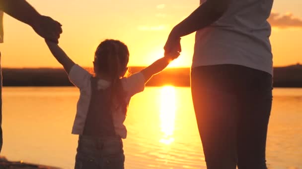 Little daughter jumping holding hands of dad and mom at sunset. Happy family life concept. A child with his parents plays together in flight. Mother and father on a walk with the kid. Spend the — Stock Video