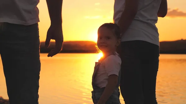 Little daughter jumping holding hands of dad and mom at sunset. Happy family life concept. A child with his parents plays together in flight. Mother and father on a walk with the kid. Spend the — Stock Photo, Image