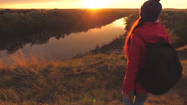 Dziewczyna zstępuje z wysokiej góry o wschodzie słońca, podnosząc ręce. Podróżniczka idzie nad rzekę. Osiągnij swoje cele na swojej drodze życia. Styl życia turysty w aktywnym — Wideo stockowe