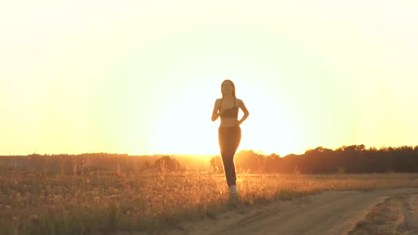 一个漂亮的姑娘穿着运动服在夕阳西下跑步.健美健美的体育活动.一个健康的女人是成功的。在胜利的道路上，实现自己的目标。往前走！ — 图库视频影像