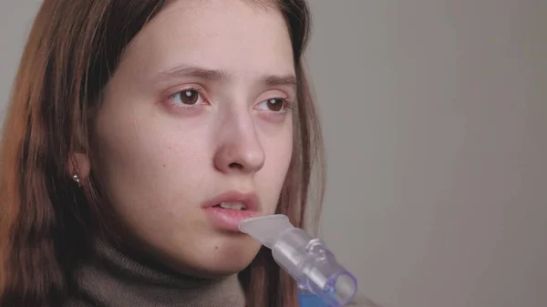 The girl breathes in a solution for inhalation of lungs. A young woman in quarantine treats a cough by inhaling steam with medicine. Treatment of a person at home with professional equipment for colds — Stock Photo, Image