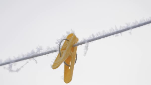 Bunte Wäscheklammern hängen bei Raureif im Winter draußen im Schnee an einem Seil — Stockvideo