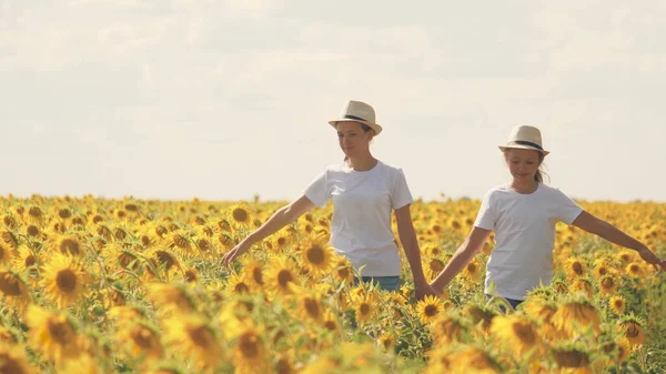 Tienermeisjes lopen over het veld met zonnebloemen en glimlach. Zomer wandelingen in bloemenbeplanting. Jeugd van boeren. Vriendinnen samen. Zaden telen voor het persen van plantaardige olie — Stockfoto