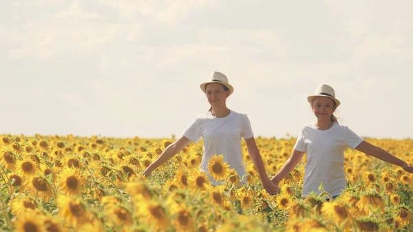 Tienermeisjes lopen over het veld met zonnebloemen en glimlach. Zomer wandelingen in bloemenbeplanting. Jeugd van boeren. Vriendinnen samen. Zaden telen voor het persen van plantaardige olie — Stockfoto