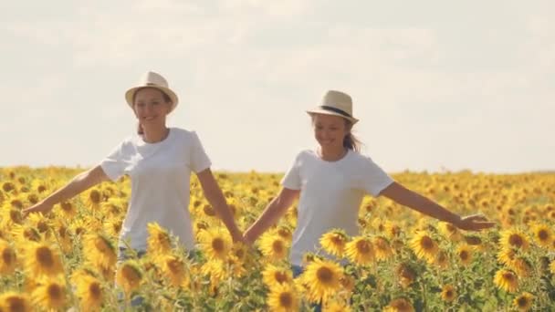 Teenager-Mädchen laufen mit Sonnenblumen über das Feld und lächeln. Sommerliche Tageswanderungen in Blumenbepflanzungen. Kindheit der Bauern. Freundinnen zusammen. Saatgut anbauen, um Pflanzenöl zu pressen — Stockvideo