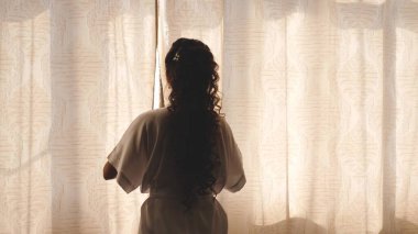 Sabahın sıcak ışığı için perdeyi çekiyorlar. Ağır çekim. Yatak odasında perdeleri açan genç bir kadın. - Yakın çekim. Sabahları eller pencerenin perdesini açar