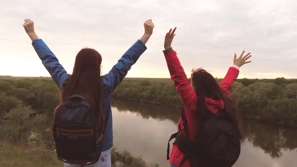 Las novias viajan con mochilas junto al río. Chicas alegres turistas están buscando aventura. Trabajo en equipo. Fin de semana en una caminata deportiva entre las mujeres. Descansa en la naturaleza. Investigación del terreno —  Fotos de Stock