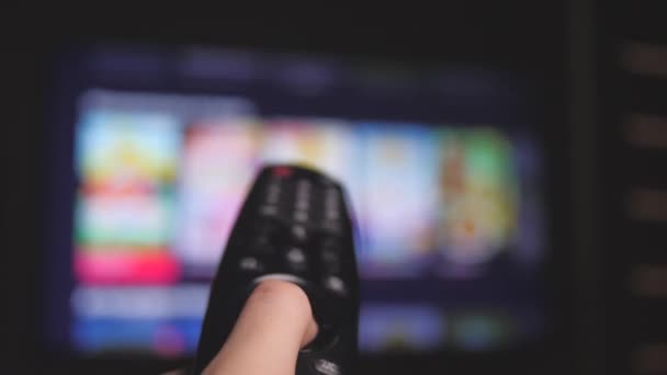 Mans mano seleziona i canali internet tv con telecomando, primo piano. La persona controlla la TV usando un moderno telecomando. Un uomo guarda la TV intelligente e usa il telecomando nero. Pagine di scorrimento tv sfocate — Video Stock