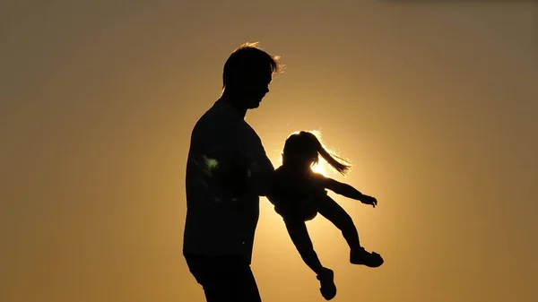 Silhouette giorno papà con figlia al tramonto. La figlia vola tra le braccia del padre con le braccia aperte ai lati. La ragazza vola in cielo tra le braccia del suo amato genitore. Separazione da — Foto Stock