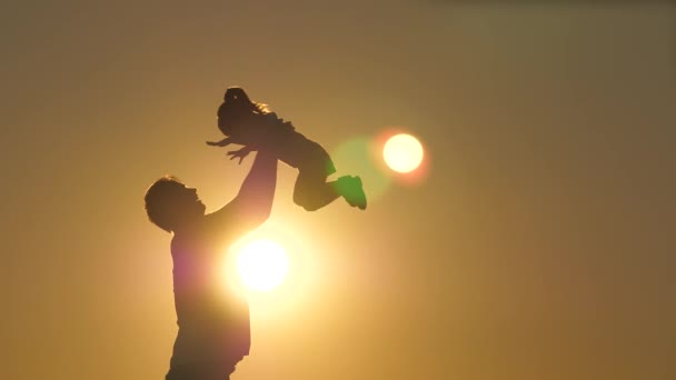 Silhouette papa jette heureuse petite fille dans le ciel couchant. La fête des pères. L'enfant veut voler au-dessus du sol. Un parent avec un enfant joue à l'aube. Concept de famille et d'enfance. Le gamin saute dessus — Video