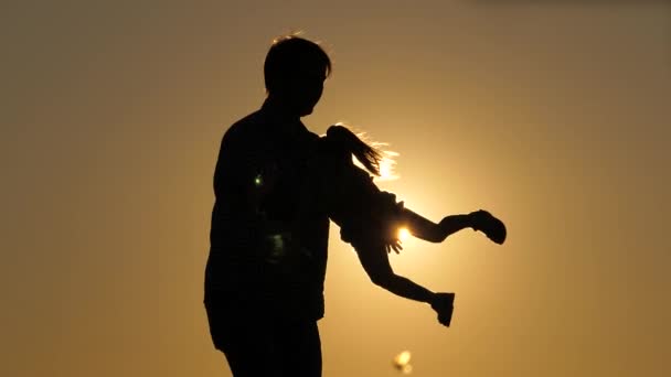 Un père aimant entoure sa petite fille qui s'envole dans les bras en l'air sur fond de ciel couchant. Silhouette d'un père et d'un enfant heureux en fuite. La vie familiale. Enfance avec un — Video