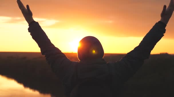 Silhouette d'un homme au coucher du soleil les mains levées contre le coucher du soleil. Un homme rêve de flotter dans les airs à bras ouverts. Rêver et prier en regardant le ciel — Video