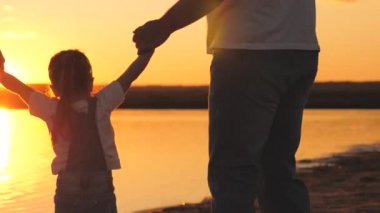 Gün batımında anne ve babanın elini tutan küçük kız. Mutlu aile hayatı konsepti. Anne ve babasıyla birlikte uçan bir çocuk. Anne ve baba çocukla yürüyüşe çıktılar. Harca