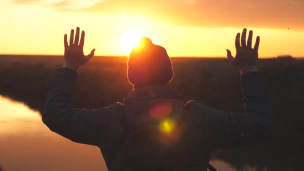 Silhouette d'un homme au coucher du soleil les mains levées contre le coucher du soleil. Un homme rêve de flotter dans les airs à bras ouverts. Rêver et prier en regardant le ciel — Video