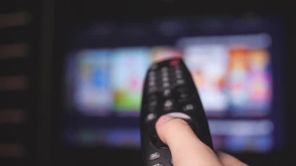 Mans mano seleziona i canali internet tv con telecomando, primo piano. La persona controlla la TV usando un moderno telecomando. Un uomo guarda la TV intelligente e usa il telecomando nero. Pagine di scorrimento tv sfocate — Video Stock