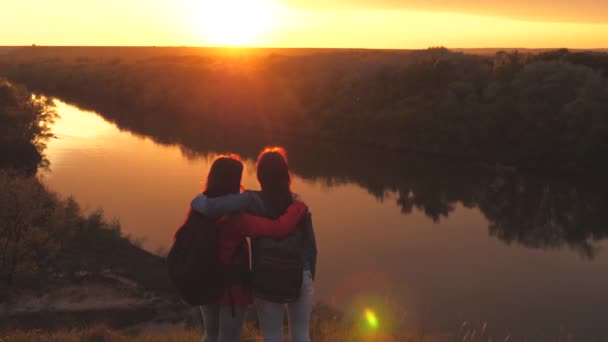 Amigos con mochilas abrazan al amanecer. Hermosas chicas se encuentran con el sol en la mañana en una alta montaña y mirar a la distancia. Las mujeres viajeras están buscando aventura. Hombre en un viaje de camping en el — Vídeos de Stock