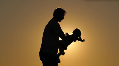 Gün batımında kızımla baba günü silueti. Kız, kollarını yanlara açmış babasının kollarında uçuyor. Kız, sevgili ailesinin kollarında gökyüzünde süzülüyor. Ayrılma