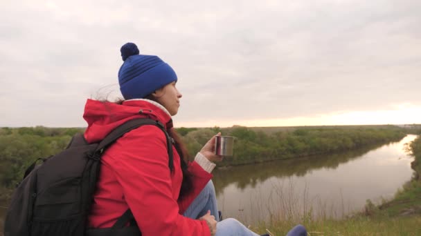 La chica bebe té de una taza sentada en lo alto de la montaña y disfrutando de la naturaleza se relaja y mira a la distancia. Un viajero en una parada en un crucero se está calentando con una bebida caliente — Vídeos de Stock