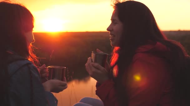 Ragazze felici amiche al tramonto cielo bere il tè da tazze su un viaggio in campeggio. I viaggiatori si stanno riposando su una pausa crogiolandosi in bevande calde e ridendo. Le donne allegre amano rilassarsi insieme all'alba. Lavoro di squadra — Video Stock