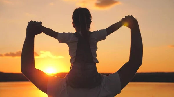 Happy daddy carries a small child on his shoulders with his hands up at sunset in the sky. Fathers day. A kid with a parent dreams of flying against the background of the morning dawn. Family life