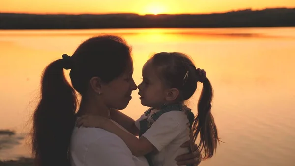 Lycklig mamma håller ett litet barn i sina armar och leker med näsan skrattande åt solnedgången på himlen. Ett lyckligt familjeliv. Mammas dag. Mor och dotter i gryningen. Grabben umgås med sin förälder. Mödrar — Stockfoto