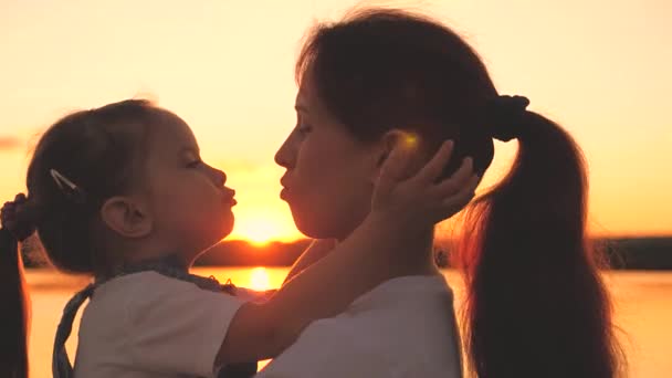Une petite fille au coucher du soleil embrasse une mère heureuse qui la tient dans ses bras. Un enfant avec sa mère bien-aimée joue à l'aube dans le ciel. Le jour des mamans. Voyager avec bébé dans l'éblouissement du soleil. Enfance avec — Video