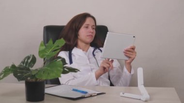 Gülümseyen genç kadın terapist dijital bilgisayar tabletinde online sağlık uygulaması kullanıyor, klinikte hasta randevusu planlıyor. Mutlu doktor pratisyen hekimin elinde dokunmatik ped var.