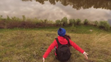 Bir kız gezgin bir sırt çantasıyla bir dağın tepesinde oturur, kolları yanlara açıktır. Genç bayan turist nehrin yanında nefes alıyor. Kendini ararken maceraya susamışsın.