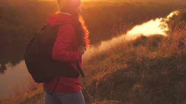 Sırt çantalı mutlu bir turist gün doğumunda dağda yürür ve gülümser. Bölgede macera seyahati arayın. Yaşam biçimi olarak yaşam biçimi. Spor gezisindeki bir kadın. Doğada özgür bir adam.