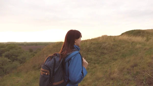 Een meisje reiziger met een rugzak op haar schouders loopt langs de rivier langs een hoge berg en glimlacht. Wandeltochten. Een mooie gratis tiener neemt een pauze van de dagelijkse drukte en studie — Stockfoto