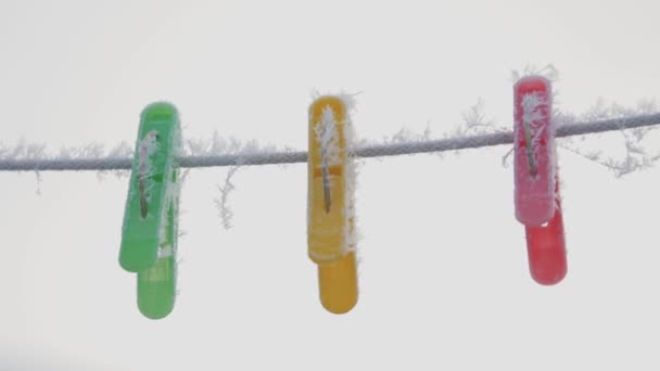 Mollette multicolore su una corda in hoarfrost appendere su una corda in inverno al di fuori nella neve — Video Stock