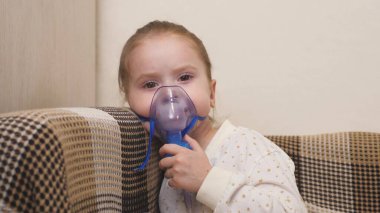 Maskeli şirin bir bebek astım spreyinden nefes alıyor. Ev solunumu prosedürü. Çocuk nebulizatörle solunum terapisi görüyor. Coronavirus 'lu çocuğu evinde tedavi et. Küçük bir kız.