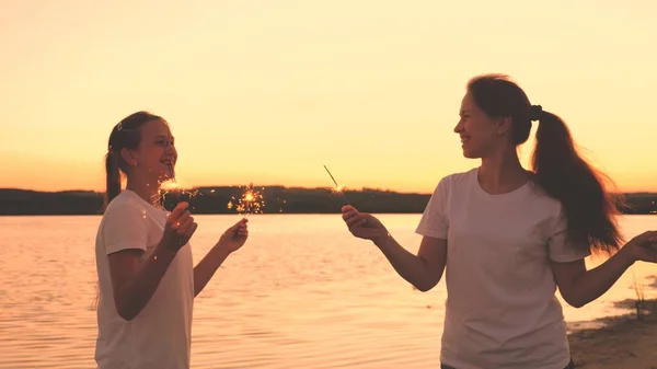 Chicas felices con bengalas bailan al atardecer en el cielo y ríen. Los jóvenes saludan al amanecer con hermosas luces. Las novias viajan. Descanse durante las vacaciones. Celebrando tu cumpleaños con diversión —  Fotos de Stock