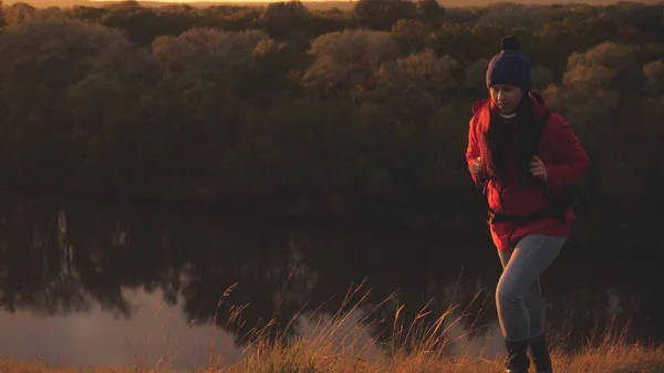 Gelukkig meisje toerist met een rugzak wandelingen op de berg bij zonsopgang en glimlacht. Zoek avontuurlijke reizen door de omgeving. Levenspad als manier van leven. Een vrouw op een sportieve wandeling. Een vrij man in de natuur — Stockfoto