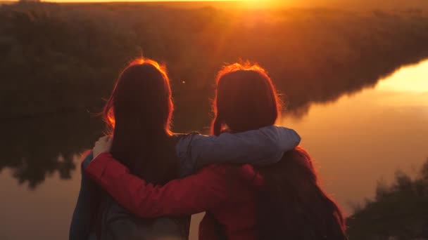 A lányok ölelkeznek naplementekor az égen. Utazó nők napkeltekor. Turista túrák a világ körül a nap fényében. Töltsd a hétvégét a szeretett családoddal a természetben. Családi élet. Csapatmunka. Közel. — Stock videók