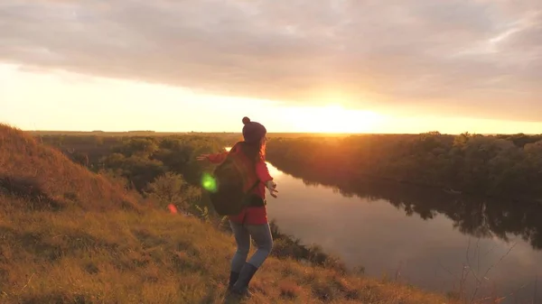 Una joven con los brazos extendidos siente libertad al atardecer. Mujer aventurera en el fondo del cielo. Trabajo de investigación con una mochila. Caminata de fin de semana. Turista en tierra. Vida alegría en —  Fotos de Stock