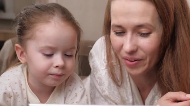 Seorang ibu dengan anak kecil berkomunikasi melalui tablet menampilkan jarak jauh dan tertawa. Ibu dan anak yang bahagia bermain bersama dengan gadget saat berbaring di tempat tidur. Kehidupan keluarga. Mengisolasi diri di rumah — Stok Video