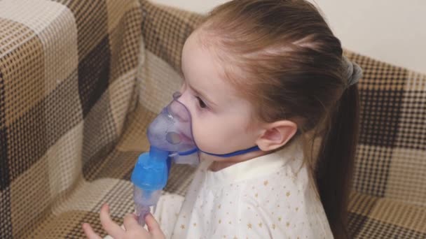 En söt bebis i mask andas genom en inhalator. Inhalationsförfarande i hemmet. Barnet får respiratorisk behandling med ett nebulisator. Behandla ditt barn för coronavirus hemma. Ett litet barn — Stockvideo