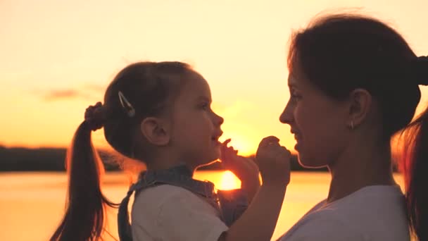 お母さんと小さな子供が空の夕日で遊んでいます。幸せな母親と娘は日の出を賞賛する。家庭生活の概念。チームワークだ。太陽のまぶしさの中で若い女性と女の子。子供への愛 — ストック動画