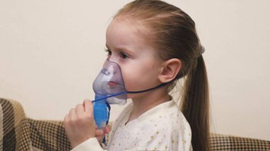 Maskeli şirin bir bebek astım spreyinden nefes alıyor. Ev solunumu prosedürü. Çocuk nebulizatörle solunum terapisi görüyor. Bebeğinize evde koronavirüs tedavisi uygulayın. Küçük bir çocuk.