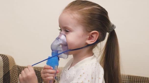 En söt bebis i mask andas genom en inhalator. Inhalationsförfarande i hemmet. Barnet får respiratorisk behandling med ett nebulisator. Behandla ditt barn för coronavirus hemma. Ett litet barn — Stockvideo