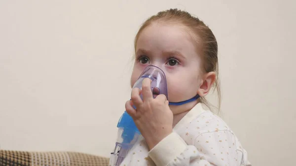 Maskeli şirin bir bebek astım spreyinden nefes alıyor. Ev solunumu prosedürü. Çocuk nebulizatörle solunum terapisi görüyor. Bebeğinize evde koronavirüs tedavisi uygulayın. Küçük bir çocuk.